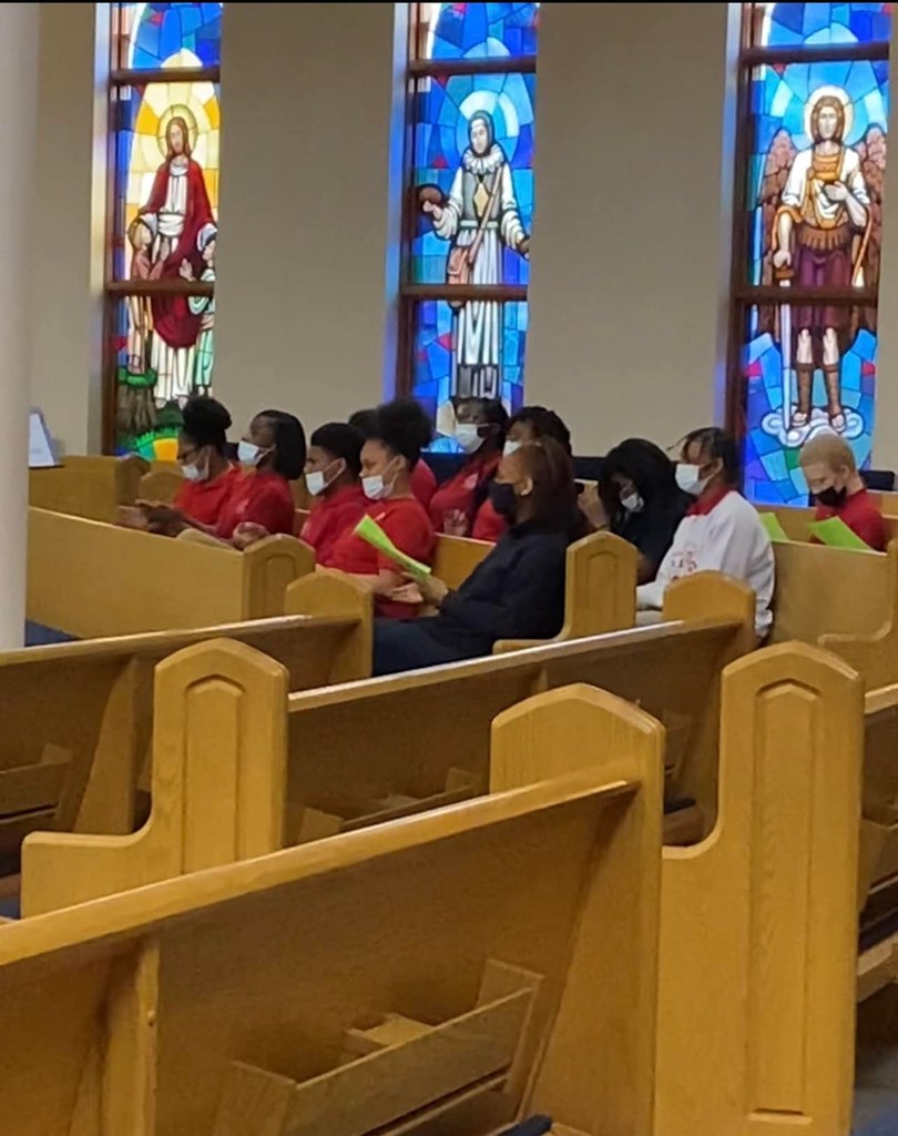 mass attendees in pews with stained glass behind them